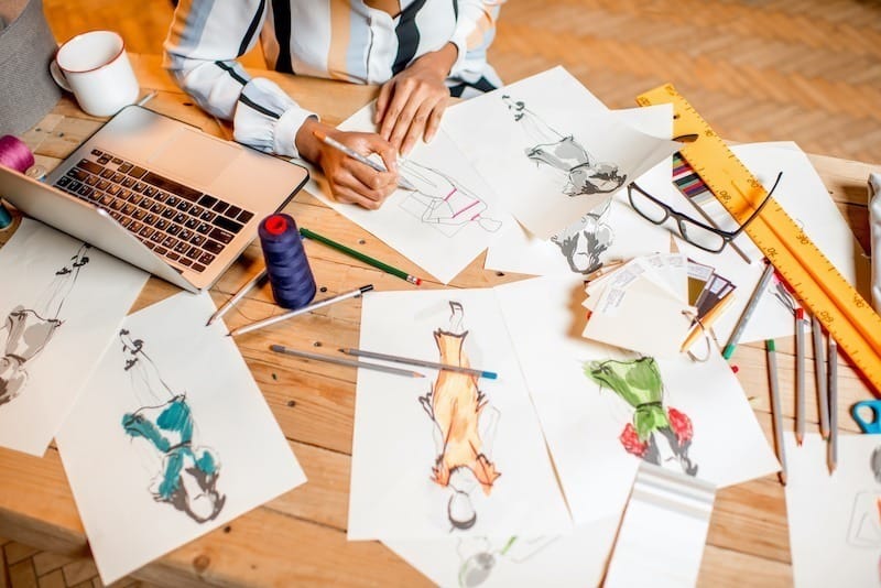Fasion designer sketching clothes drawings at the table with tailoring tools and laptop